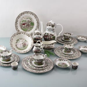 Könnte beinhalten: Ein Set aus weißem Porzellan-Geschirr mit einem grün-braunen Blumenmuster. Das Set enthält Teller, Schalen, Tassen, Untertassen, eine Teekanne, eine Milchkännchen und eine Zuckerdose.