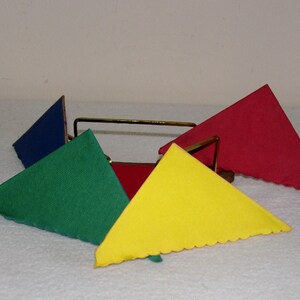 May include: A set of four triangular napkins in red, blue, green, and yellow, folded and displayed in a metal napkin holder.