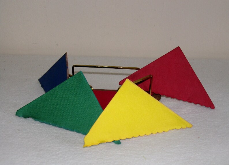 May include: A set of four triangular napkins in red, blue, green, and yellow, folded and displayed in a metal napkin holder.