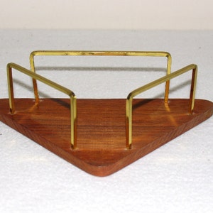 May include: A triangular wooden napkin holder with a gold metal frame. The holder has a natural wood finish and the frame is made of thin, polished metal.