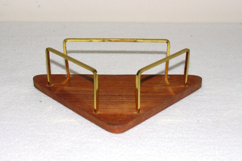 May include: A triangular wooden napkin holder with a gold metal frame. The holder has a natural wood finish and the frame is made of thin, polished metal.