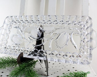 May include: A clear glass serving tray with a floral design. The tray has a diamond pattern around the edge and two handles.
