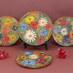 May include: Four round wooden coasters with hand-painted floral designs in bright colors, including red, yellow, blue, green, and white.