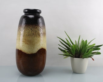 May include: A brown, yellow, and black ceramic vase with a textured surface. The vase is tall and narrow, with a rounded bottom and a flared top.