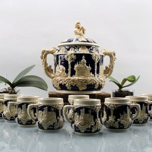 May include: A set of 10 ceramic mugs and a large ceramic punch bowl with a blue and white design. The mugs and bowl feature a raised design of a castle and trees.
