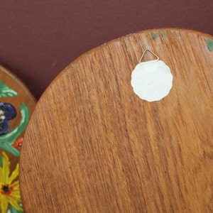 May include: The back of a round wooden wall hanging with a white paper circle attached with a metal hook. The wood has a natural grain pattern.