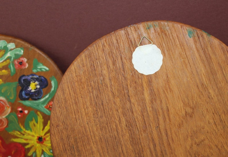 May include: The back of a round wooden wall hanging with a white paper circle attached with a metal hook. The wood has a natural grain pattern.