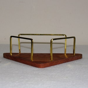 May include: A triangular wooden tray with a gold metal frame. The tray has a dark wood grain and the frame is made of thin, rectangular bars.