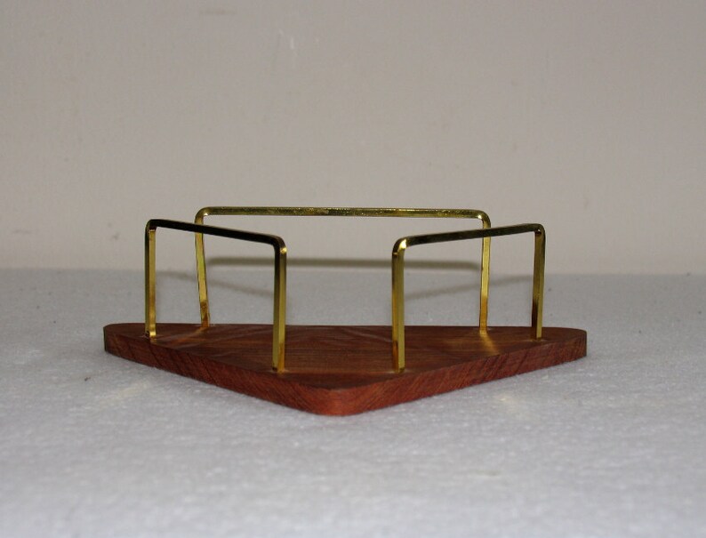 May include: A triangular wooden tray with a gold metal frame. The tray has a dark wood grain and the frame is made of thin, rectangular bars.