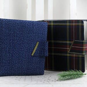May include: Two fabric-covered binders, one blue with a subtle texture and one black with a red and green plaid pattern. Both binders have a gold metal closure.