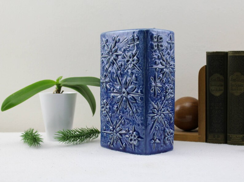 May include: A blue ceramic vase with a geometric pattern of stars. The vase is rectangular and has a smooth, glazed finish.