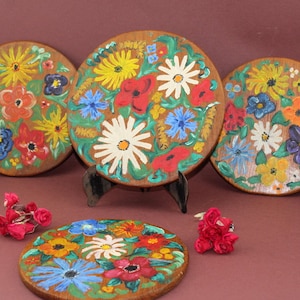May include: Four round wooden plates with hand-painted floral designs. The plates feature a variety of colorful flowers, including red, yellow, blue, and white.