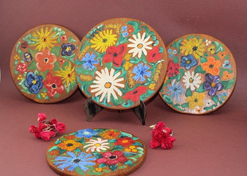 May include: Four round wooden plates with hand-painted floral designs. The plates feature a variety of colorful flowers, including red, yellow, blue, and white.