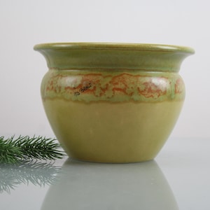 May include: A green and yellow ceramic planter with a brown glaze. The planter has a rounded shape and a wide rim.