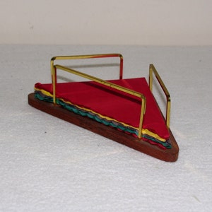 May include: A wooden napkin holder with a gold metal frame. The holder is filled with multi-colored napkins, including red, green, yellow, and brown.