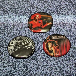 Könnte beinhalten: Drei runde Ansteckbuttons mit Bildern aus der Fernsehserie Twin Peaks. Einer zeigt eine Frau in Rot, ein anderer hat ein schwarz-weißes Zickzackmuster, und der dritte hat den Text "Twin Peaks Fire Walk With Me".