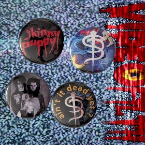 May include: Four round buttons with various designs. One button has the text "Skinny Puppy" in red on a black background. Another features a band photo in black and white. The other two buttons have graphic designs and text.