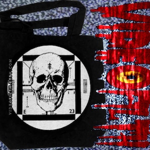 Peut inclure: Sac fourre-tout noir avec un graphique circulaire blanc d'un crâne à l'intérieur d'un motif de test de télévision. Le texte "VIDEOFILTH.ETSY.COM" est imprimé sur le côté du sac.