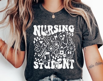 May include: A dark gray t-shirt with a white graphic design that says "Nursing Student" and features a variety of medical symbols and icons.