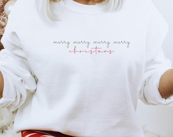 May include: A white crewneck sweatshirt featuring the text merry merry merry merry christmas in black and red cursive lettering. The garment has long sleeves and a ribbed neckline, cuffs, and hem, providing a clean and simple aesthetic.