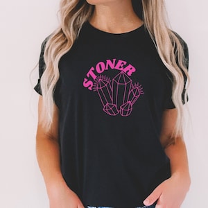May include: A black t-shirt with a pink graphic of crystals and the word "STONER" in pink retro lettering.