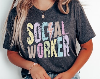 May include: A dark gray t-shirt with the words "SOCIAL WORKER" printed in colorful, distressed letters. The letters are in shades of pink, yellow, blue, and green.
