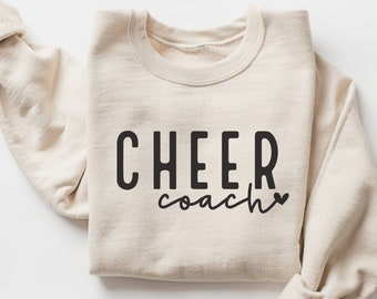 May include: A beige sweatshirt with the text "CHEER coach" in black lettering and a small heart.