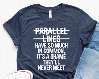 Op de afbeelding: Een marineblauw t-shirt met witte tekst die "PARALLEL LINES HAVE SO MUCH IN COMMON, IT'S A SHAME THEY'LL NEVER MEET" luidt. Het shirt wordt gecombineerd met een blauwe jeans en witte sneakers.