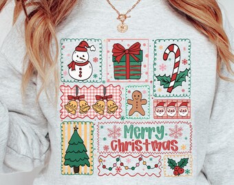 May include: A light gray sweatshirt featuring a colorful Christmas-themed graphic. The design includes a snowman, gift, candy cane, bells, gingerbread man, Santa faces, Christmas tree, and the words "Merry Christmas".