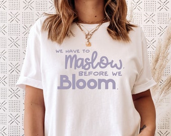 May include: White t-shirt with the text "We have to Maslow before we Bloom." printed in purple.
