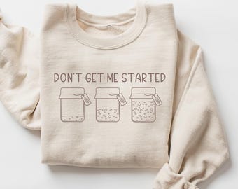 May include: A beige sweatshirt with the text "Don't get me started" and a graphic of three jars with lids. Each jar has a label that says "Good Vibes Only".