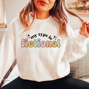 May include: A white sweatshirt with the text "my type is fictional" in rainbow colors. The text is in a retro font style.