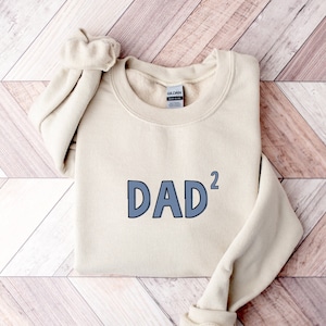 May include: A beige sweatshirt with the text "DAD²" in blue lettering.