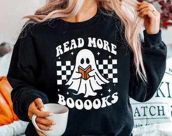 May include: Black sweatshirt with a white ghost reading a book and the text "Read More Booooks" in white. The ghost is on a checkered background with white stars.