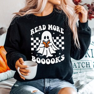 May include: Black sweatshirt with a white ghost reading a book and the text "Read More Booooks" in white. The ghost is on a checkered background with white stars.