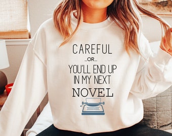 May include: White sweatshirt with the text "Careful... or... You'll end up in my next novel" and a vintage typewriter graphic.