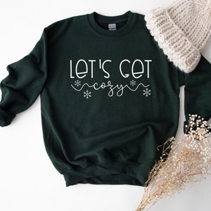 May include: A dark green sweatshirt with the text "Let's get cozy" in white lettering with snowflake accents.