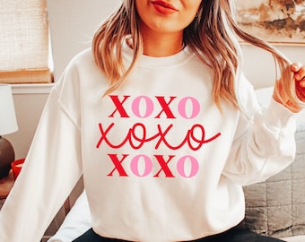 May include: White sweatshirt with the text "XOXO XOXO XOXO" in pink and red lettering.