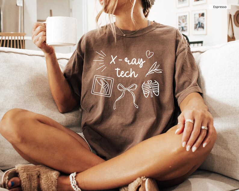 K&ouml;nnte beinhalten: Ein braunes T-Shirt mit dem Text "X-ray tech" und Illustrationen von medizinischen Ger&auml;ten, darunter ein Herz, Lungen und ein Knie.