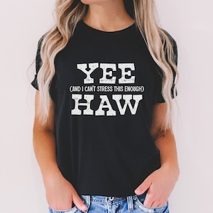Op de afbeelding: Zwart T-shirt met witte tekst die "YEE (AND I CAN'T STRESS THIS ENOUGH) HAW" zegt