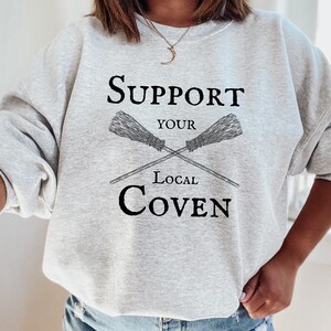 May include: Gray sweatshirt with the text "Support Your Local Coven" and a graphic of two crossed brooms.