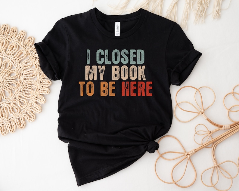 Puede incluir: Camiseta negra con un gr&aacute;fico de estilo vintage que dice "Cerr&eacute; mi libro para estar aqu&iacute;".