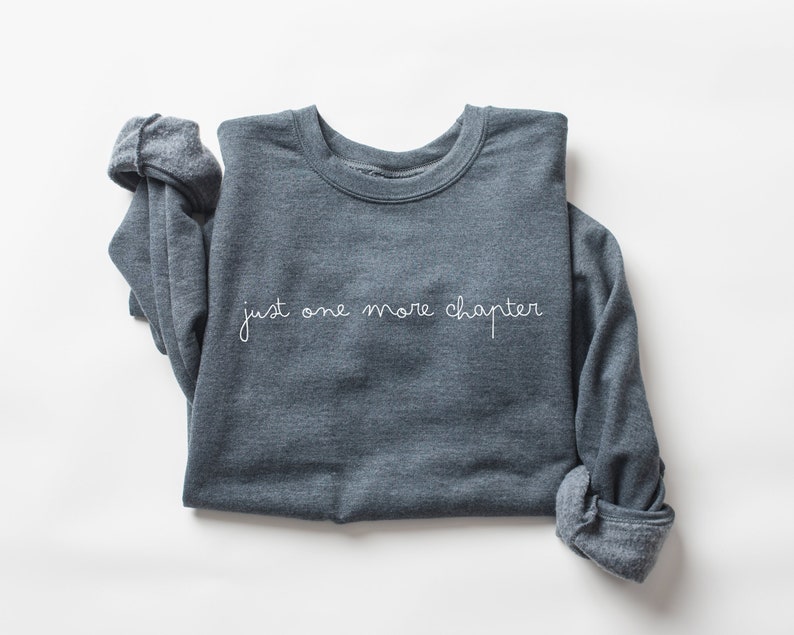 May include: A dark gray sweatshirt with the text "just one more chapter" in white lettering.