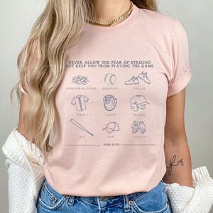 Peut inclure: Un t-shirt rose avec un motif sur le th&egrave;me du baseball. Le motif pr&eacute;sente une citation de Babe Ruth&nbsp;: &laquo;&nbsp;Ne laissez jamais la peur de frapper un home run vous emp&ecirc;cher de jouer&nbsp;&raquo;. Le motif comprend &eacute;galement des illustrations d&rsquo;&eacute;quipements de baseball, notamment une batte, une balle, un gant, une casquette, des crampons et des graines de tournesol.