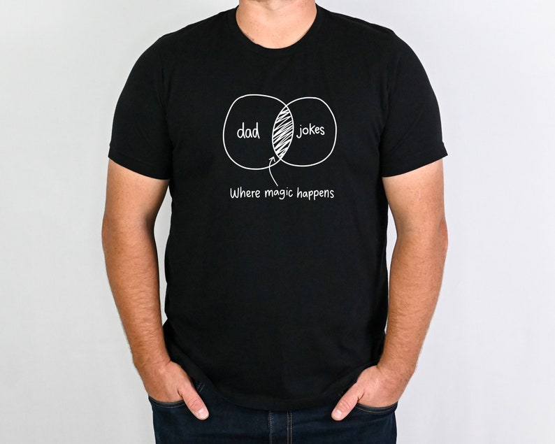 May include: A black t-shirt with a white graphic of two overlapping circles labeled "dad" and "jokes". The overlapping section of the circles is labeled "Where magic happens".