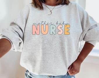 May include: Gray sweatshirt with the text "mother baby NURSE" in colorful letters. The letters are outlined in black and have a pastel color scheme.
