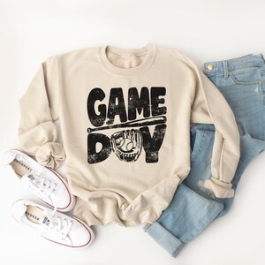 May include: A beige sweatshirt with a black graphic print that says "GAME DAY" with a baseball bat and glove.