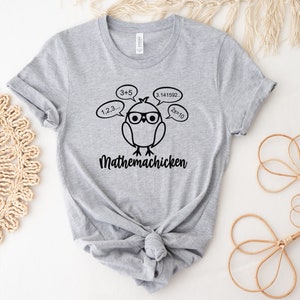 May include: Gray t-shirt with a black graphic of a cartoon chicken wearing glasses and thinking about math equations. The text "Mathemachicken" is below the chicken.