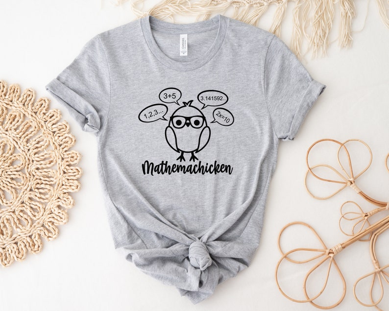 May include: Gray t-shirt with a black graphic of a cartoon chicken wearing glasses and thinking about math equations. The text "Mathemachicken" is below the chicken.