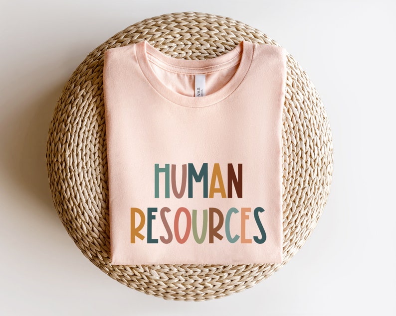 May include: A light pink t-shirt with the text "HUMAN RESOURCES" in colorful, stylized letters.